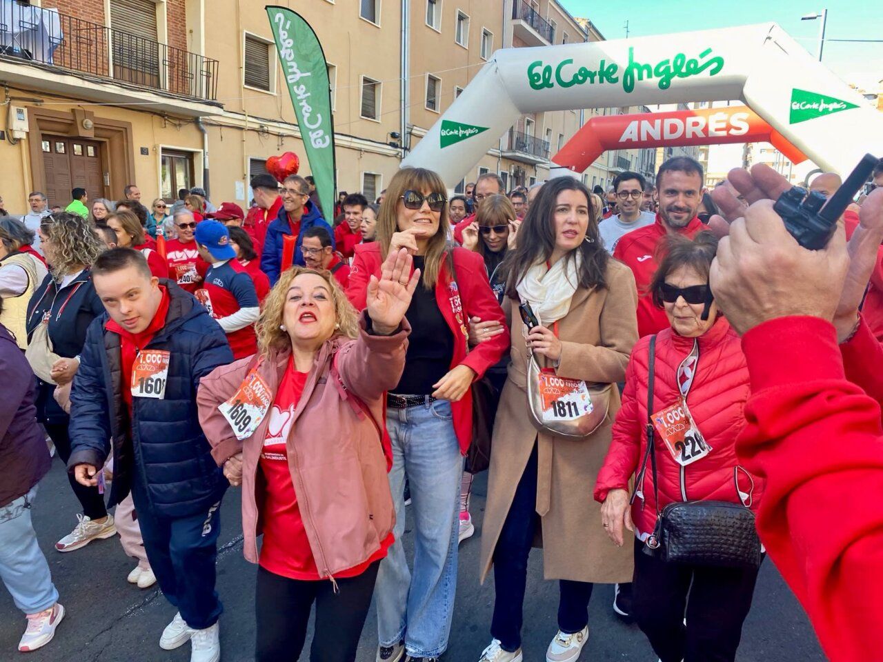 Participantes con dorsales se reúnen bajo un arco en una calle urbana.