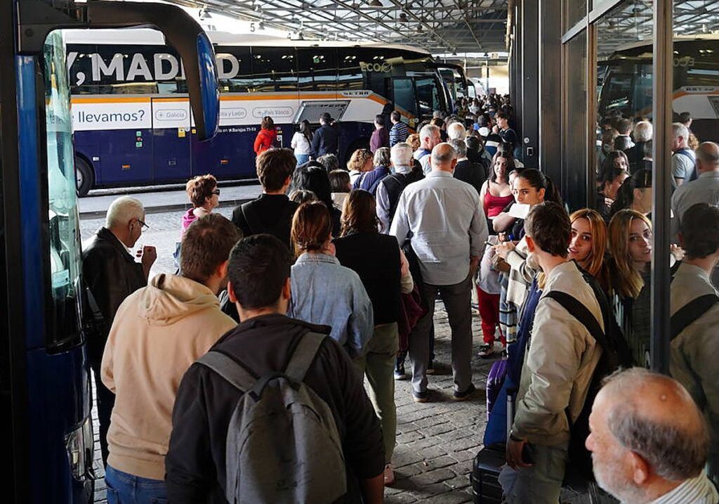 Pasajeros esperan junto a varios autobuses en una estación abarrotada.