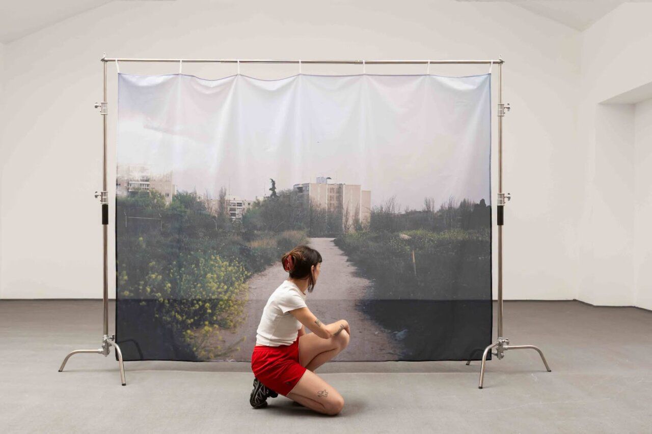 Persona arrodillada ante una gran imagen de un camino, instalada en una sala.