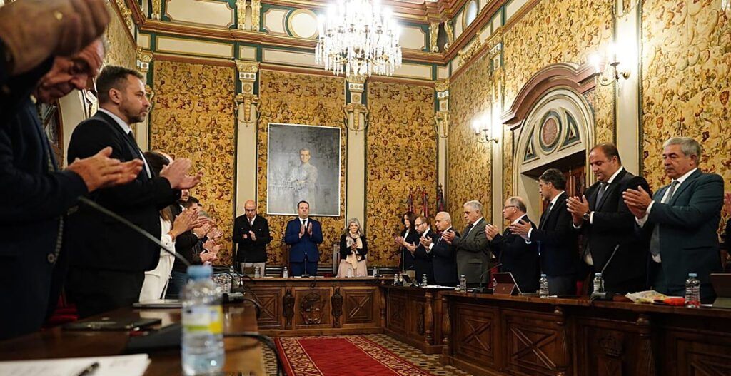 Varias personas de pie aplauden alrededor de una mesa en una sala ornamentada.
