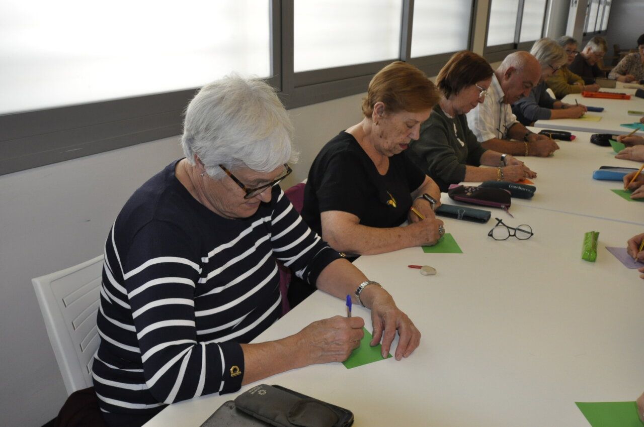 Varias personas mayores escriben en papeles de colores alrededor de una mesa.