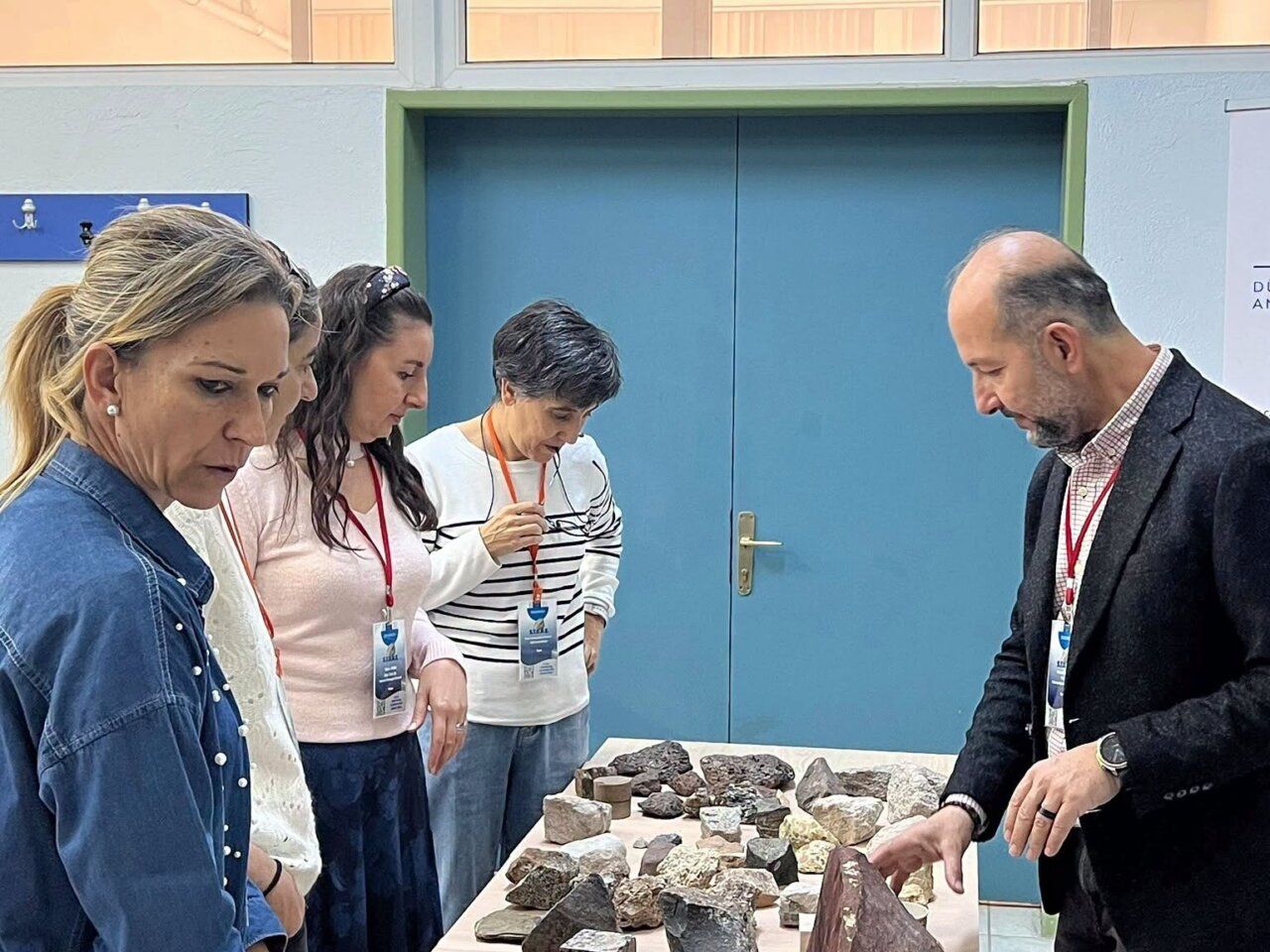 Cuatro personas observan varias muestras de roca dispuestas sobre una mesa en una sala.