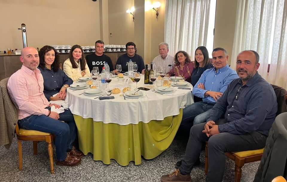 Varias personas sentadas alrededor de una mesa preparada con platos, vasos y botellas