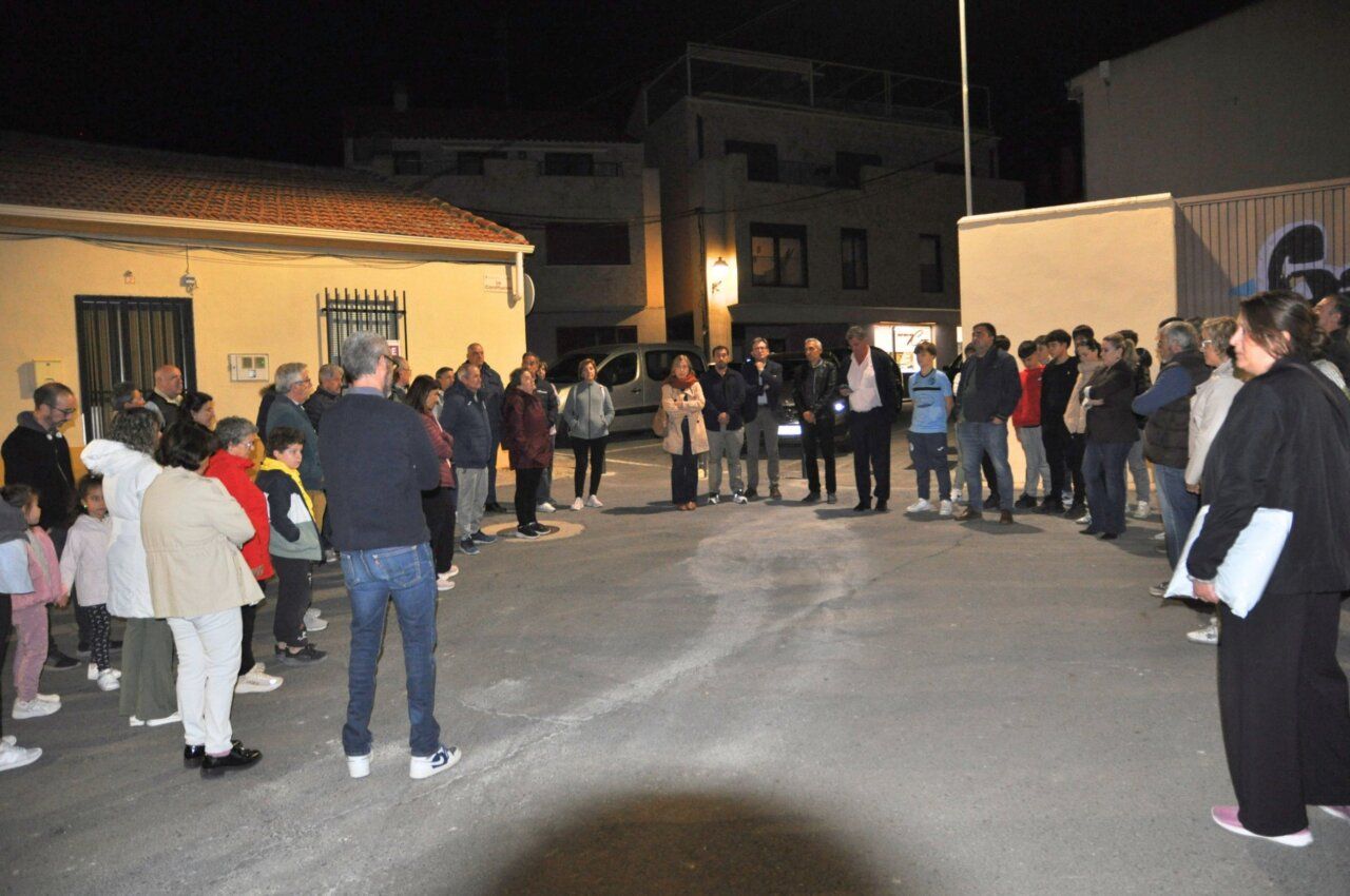 Varias personas reunidas en semicírculo en una plaza iluminada durante la noche