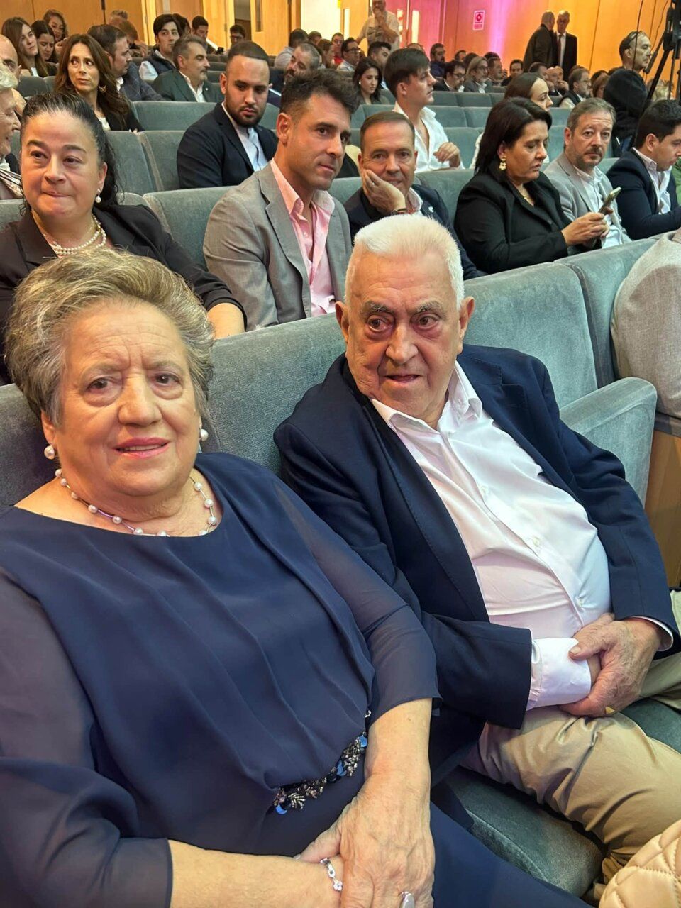 Asistentes sentados en butacas durante un acto en un auditorio.