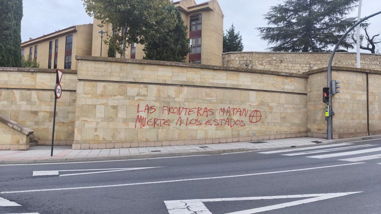 Pintada roja en un muro de piedra junto a una calle urbana.