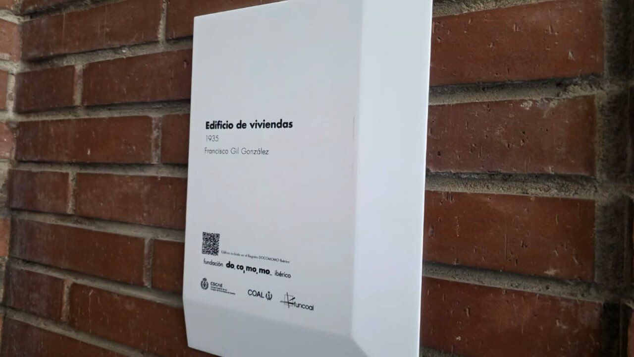 Placa blanca sobre pared de ladrillo con datos de un edificio de viviendas