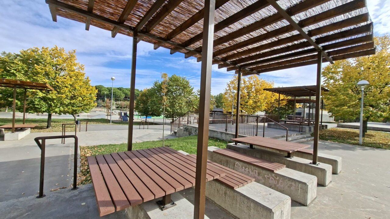Plaza al aire libre con pérgolas de madera, bancos y árboles otoñales.