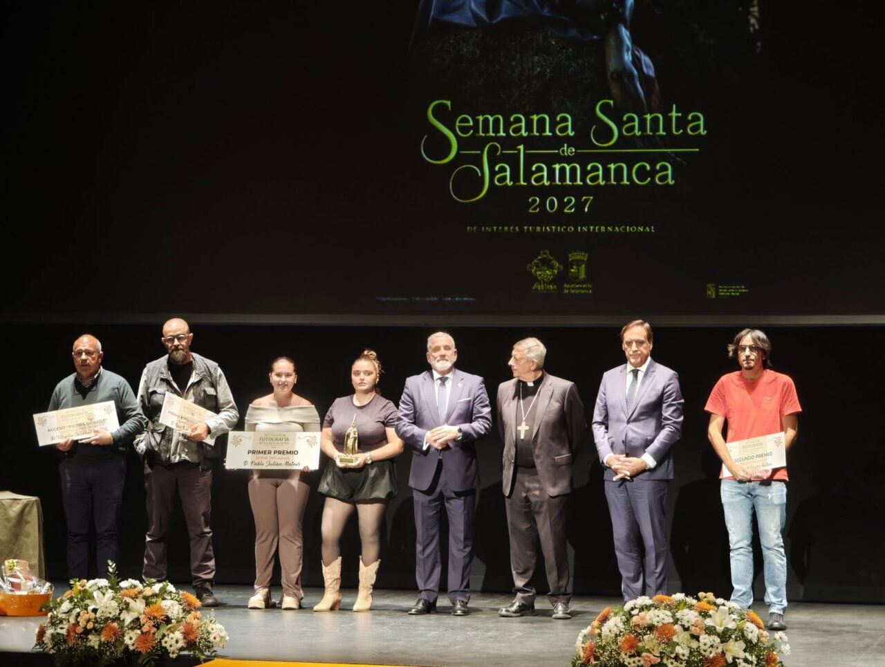 Grupo de personas posa en un escenario con diplomas y un trofeo.