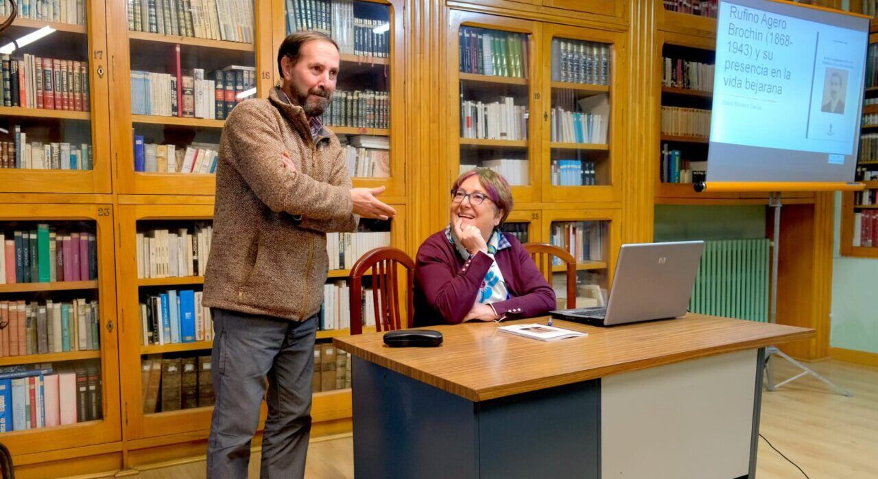 Dos personas durante una presentación, con libros y una diapositiva sobre Rufino Agero Brochín.