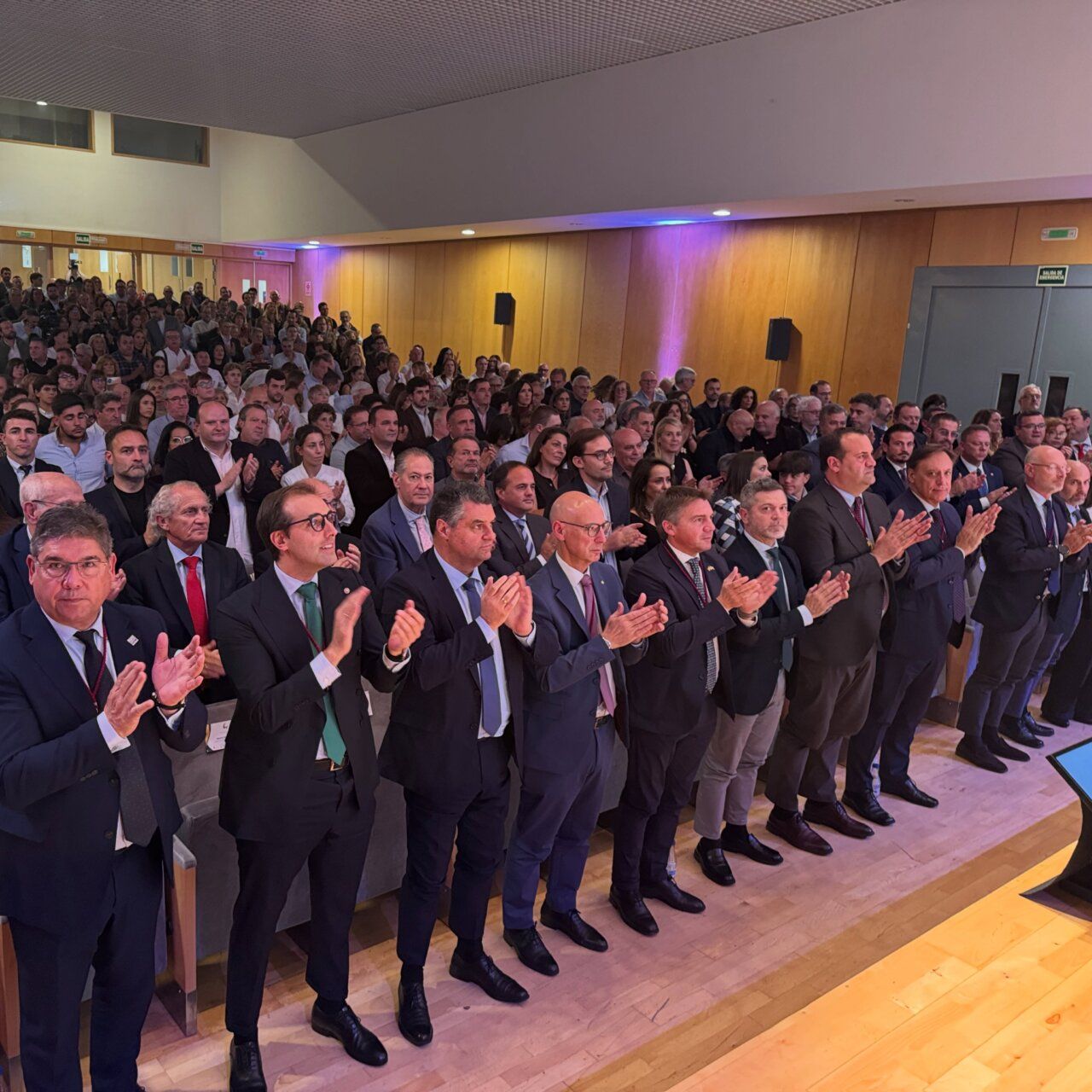 Público de pie aplaude en una sala mientras otras personas permanecen sentadas.