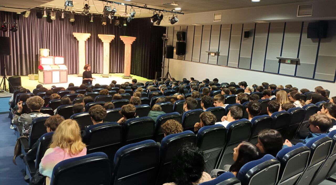 Escolares sentados en butacas miran un escenario preparado en una sala de teatro