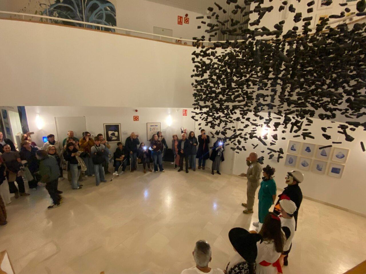 Visitantes observan una instalación suspendida en una sala de museo junto a personas disfrazadas.