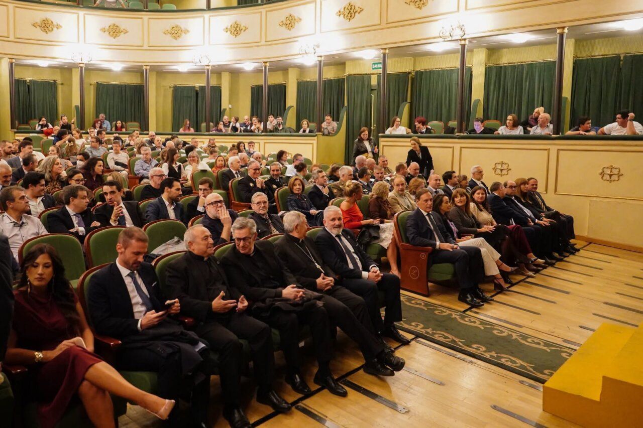 Público sentado en las butacas verdes de un teatro ornamentado.