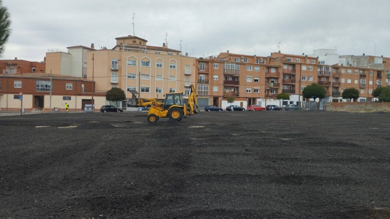 Una máquina de obra trabaja sobre un solar despejado frente a varios edificios residenciales.