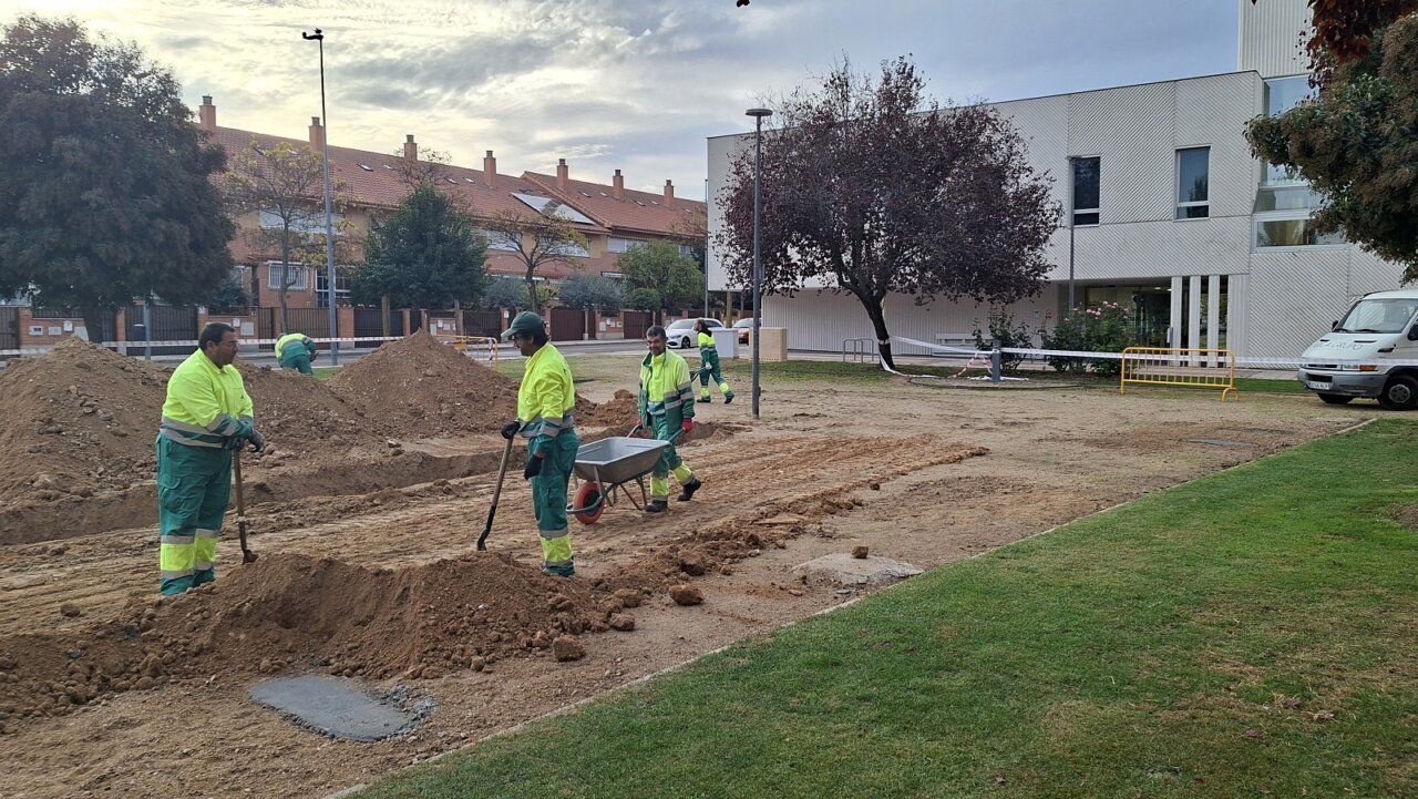 Personas trabajan en una zona de tierra junto a un edificio moderno