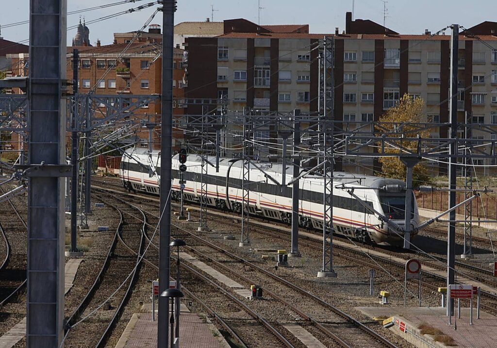Un tren blanco circula por varias vías electrificadas junto a edificios residenciales.