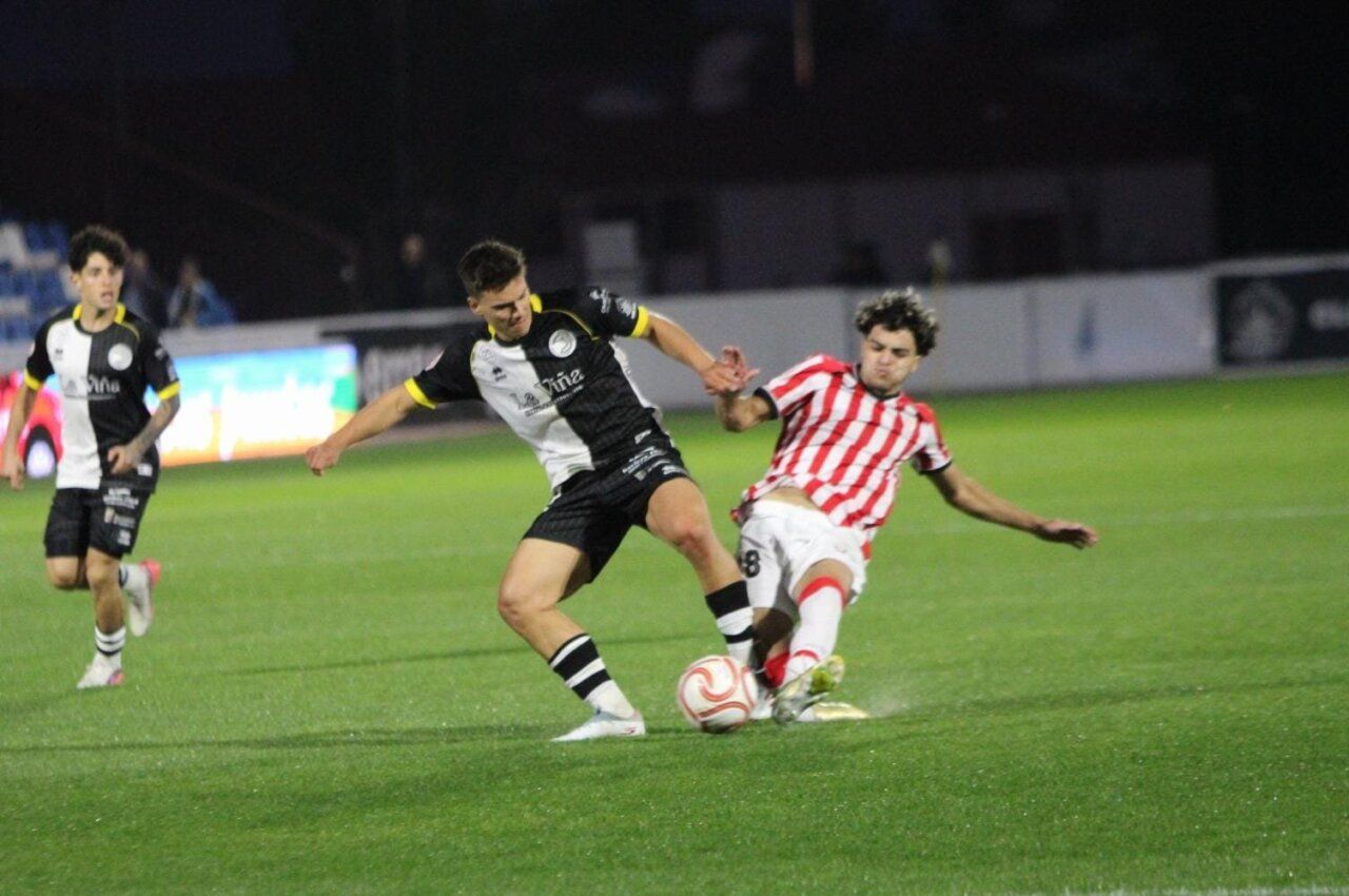 Futbolistas disputan el balón sobre el césped durante un partido de fútbol.